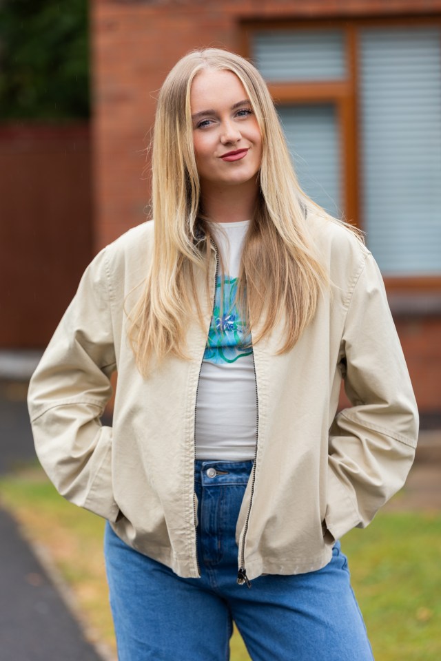 Yasmin Davies smiling at the camera, wearing a cream jacket, white top, and blue jeans.