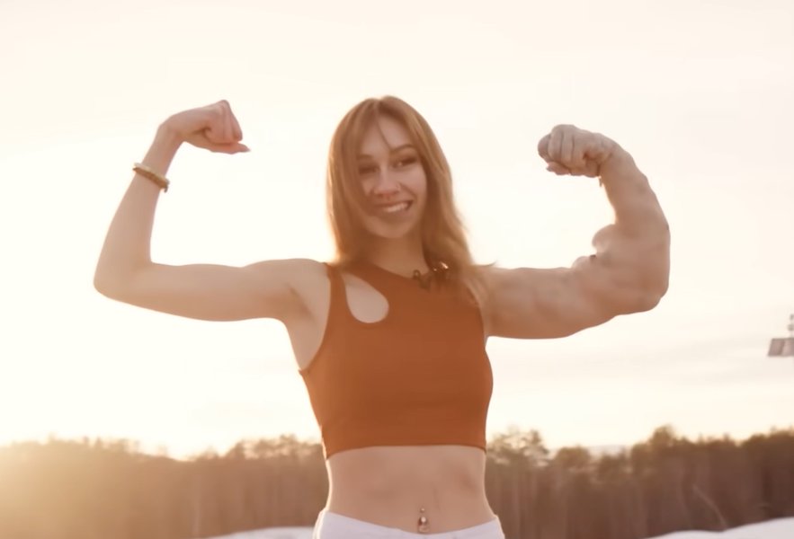 A young woman flexes her biceps, with one arm significantly more muscular than the other.