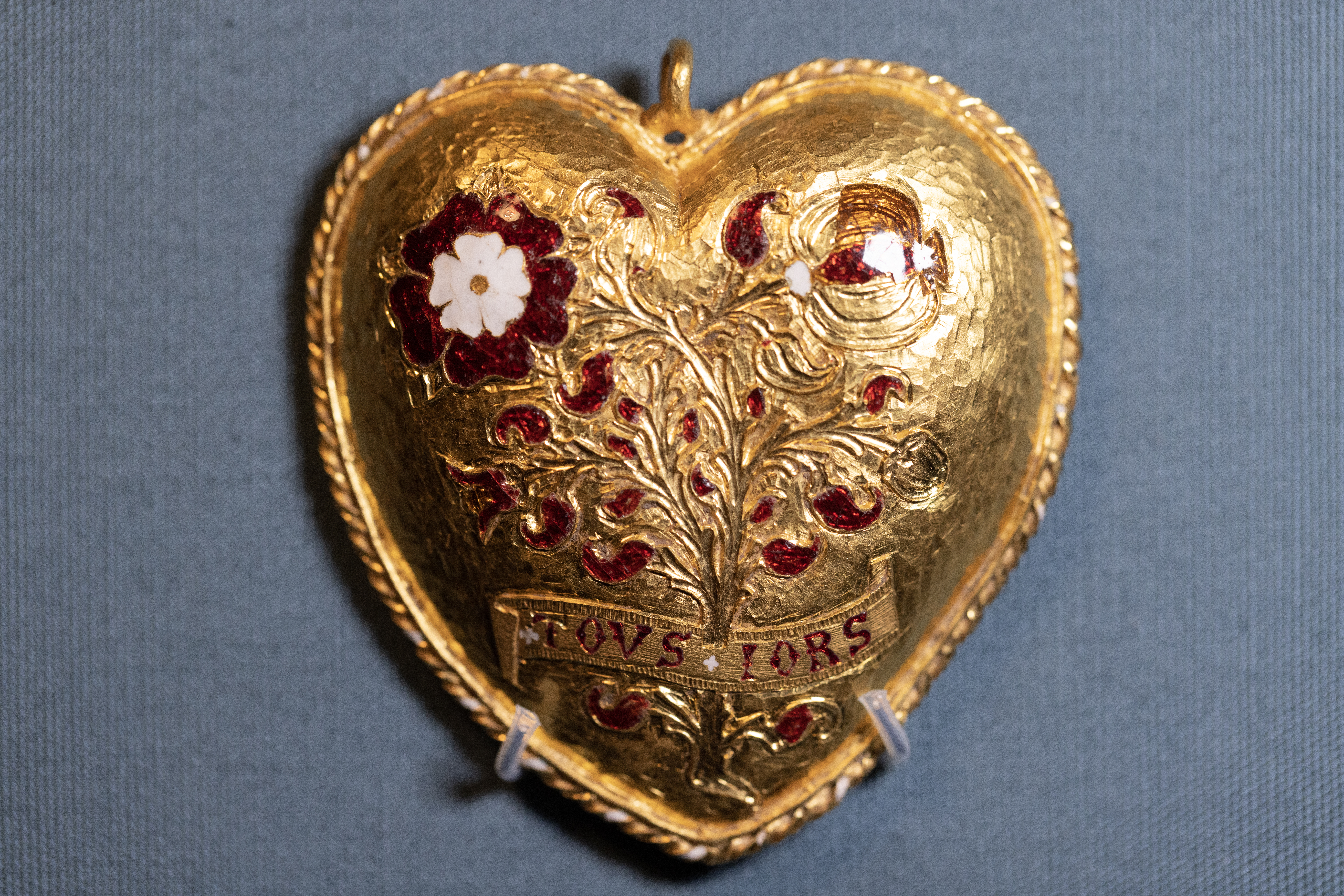 Gold heart-shaped pendant with a white Tudor rose and the words "TOVS IORS" (always) in red enamel.