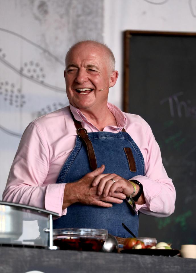 Rick Stein in a pink shirt and blue apron, smiling during a cooking show.