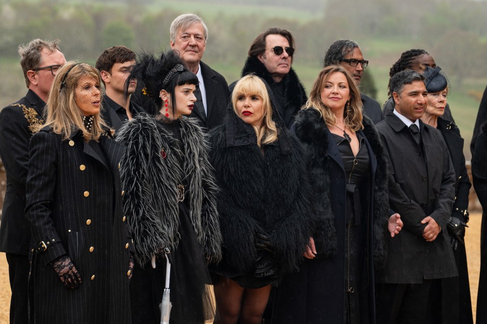 A group of people wearing black attire, including fur coats, standing outside in the rain.