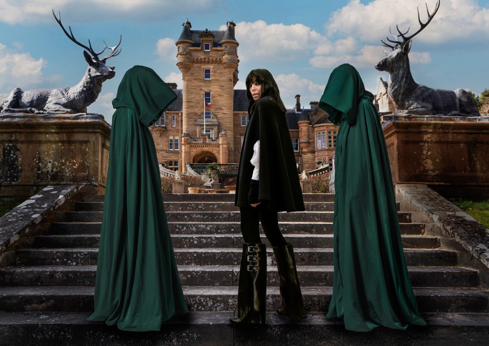 Claudia Winkleman posing in front of a castle, flanked by two figures in green cloaks and two stag statues.