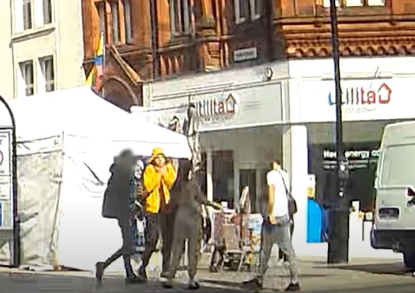 People interacting on a street with tents and buildings in the background.