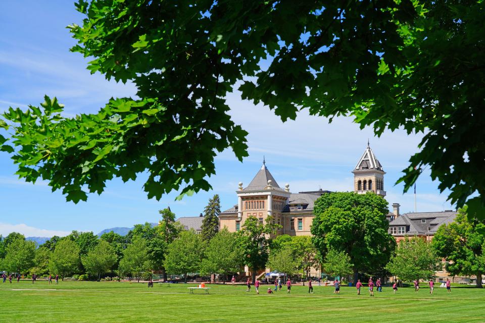 View of the Utah State University campus in Logan, Utah, with students on a green lawn and mountains in the background.