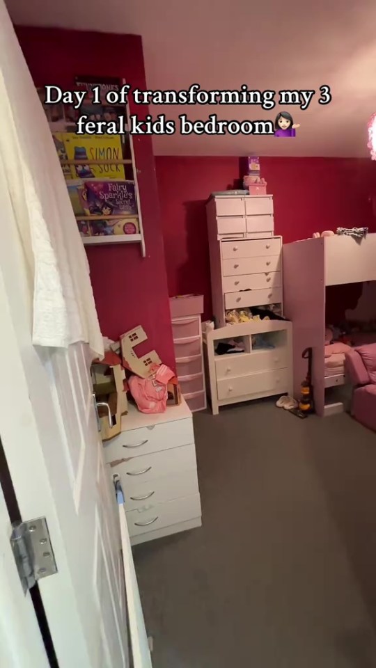 A messy kids' bedroom with pink walls, white furniture, a bunk bed, and a wall shelf with books, captioned "Day 1 of transforming my 3 feral kids bedroom."