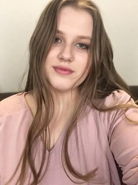 Young woman with long brown hair, wearing a pink top.