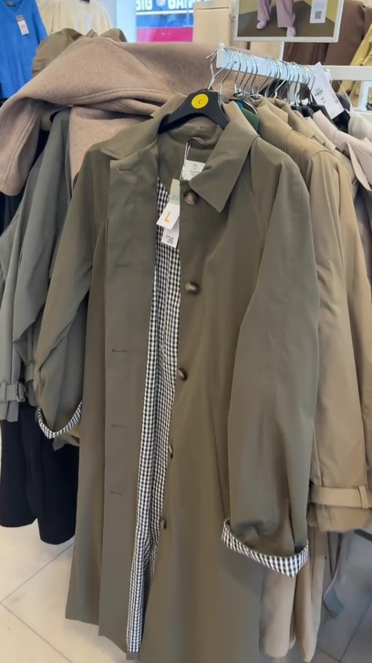 A green trench coat with a black and white checkered lining hanging on a rack.