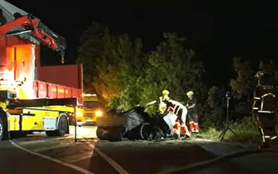 Rescuers attending to a severely damaged black Tesla after a fatal crash at night.