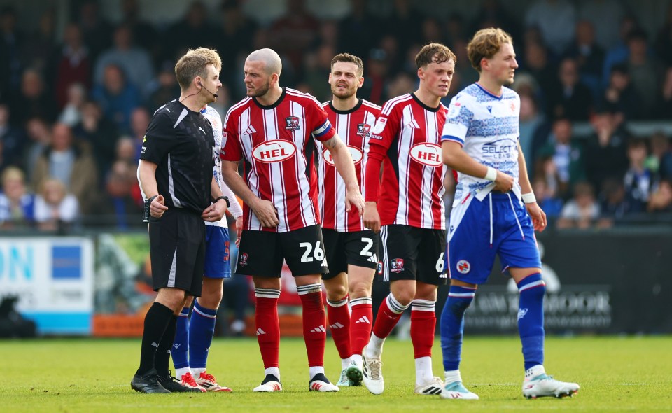 Referee James Durkin talking to Exeter City and Reading players during a soccer match.