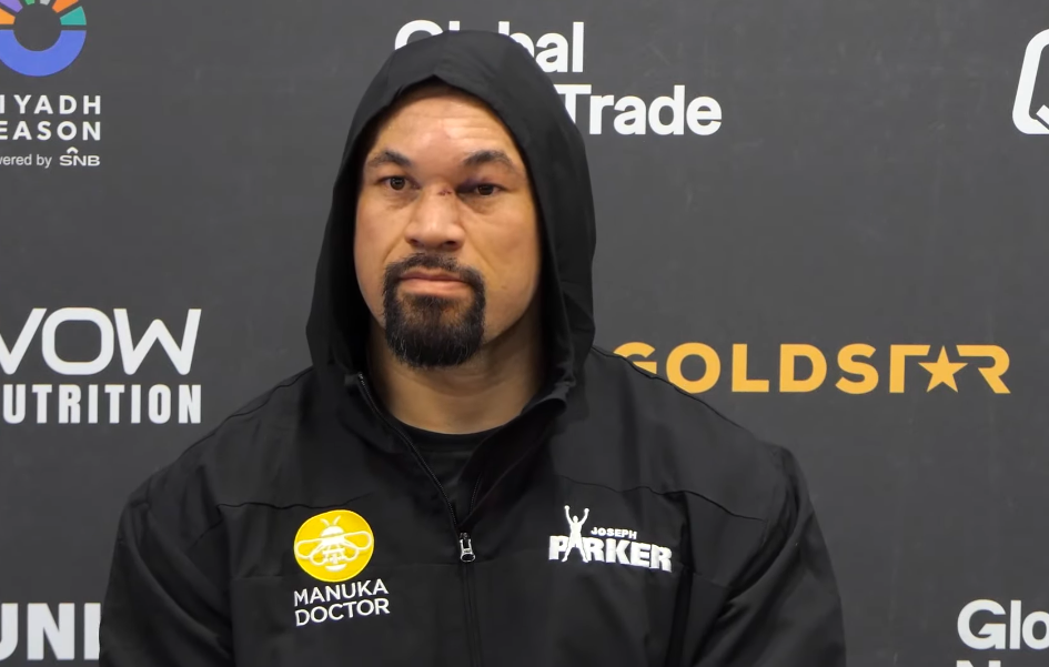 Joseph Parker, wearing a black hooded jacket with "Manuka Doctor" and "Joseph Parker" logos, stands in front of a dark background with various company logos.