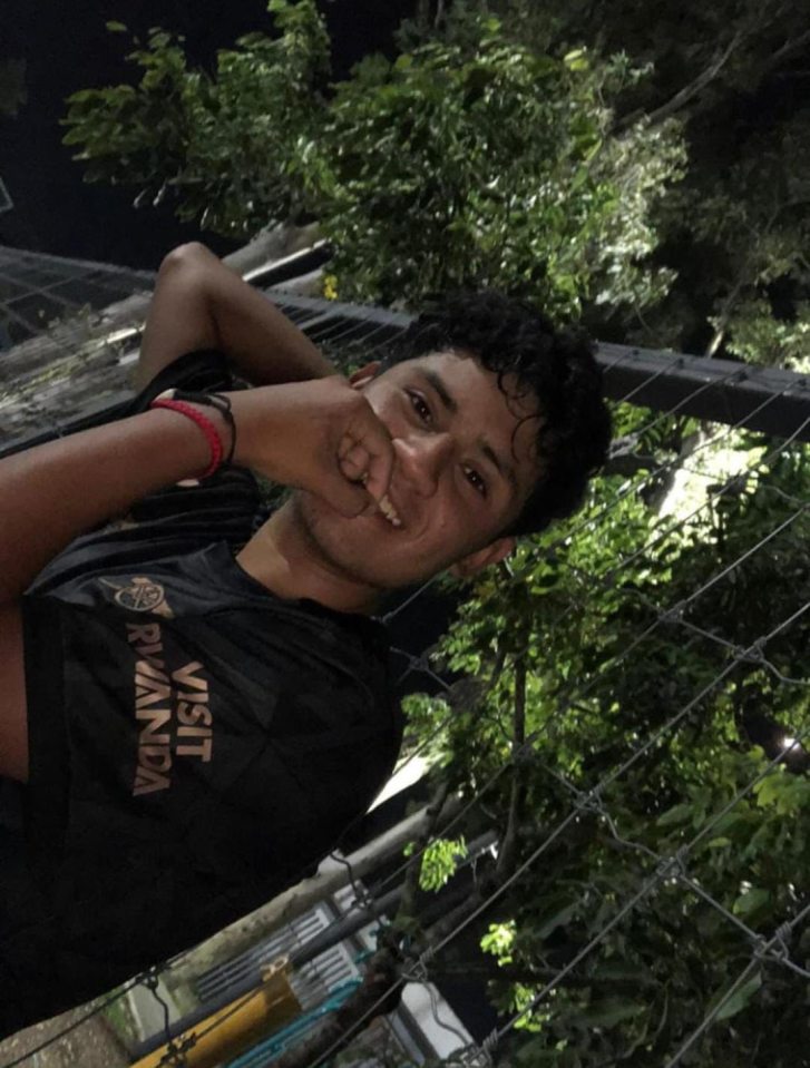 Luis Torres in a black "VISIT RWANDA" t-shirt, smiling while holding his fist to his chin.