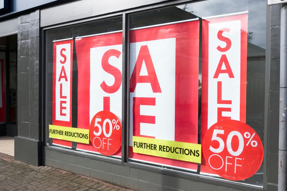 Shop window with red and white "SALE" signs, with "up to 50% OFF" and "FURTHER REDUCTIONS" banners.