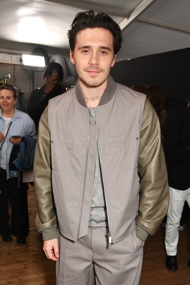 Brooklyn Beckham attending the Dior Homme Menswear Spring/Summer 2025 show in a gray bomber jacket and matching pants.