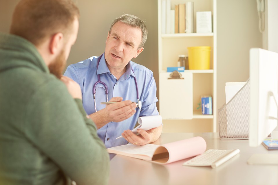 Doctor explaining something to a male patient while writing a prescription.