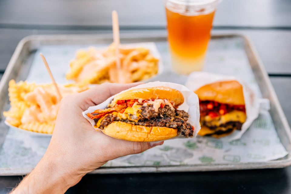 Person eating a double cheeseburger with bacon from a fast-food joint.
