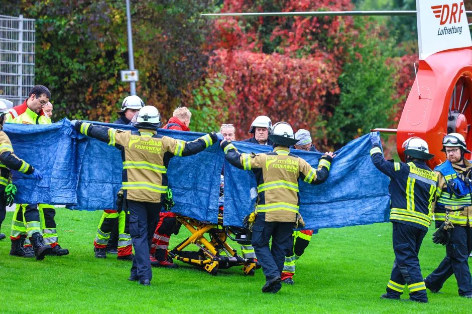 Firefighters and medical personnel using a blue tarp to shield a stretcher.