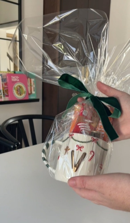 Hands holding a gift-wrapped Christmas mug filled with treats.