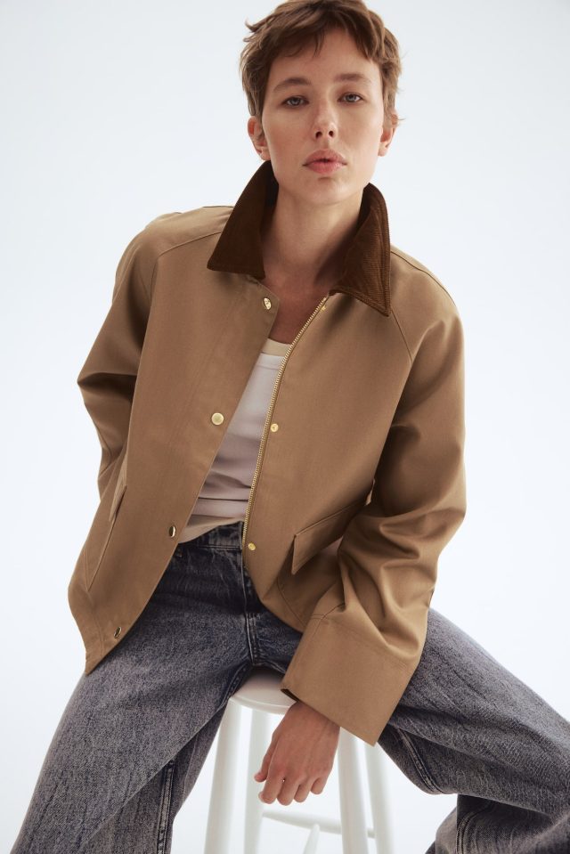 A model wearing a tan corduroy-collar jacket, white tank top, and faded blue jeans.