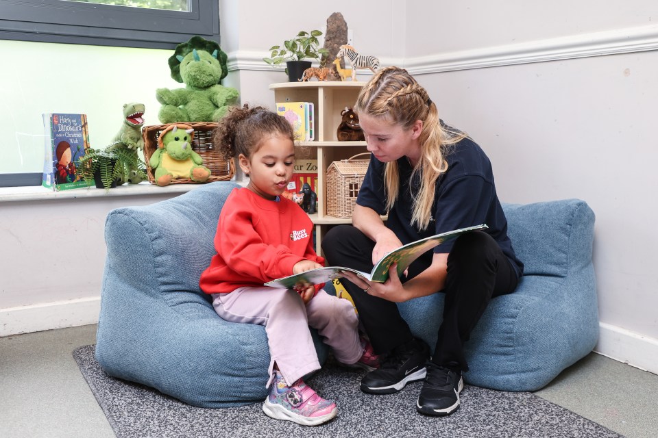 A teacher and child reading a book together in a nursery school.