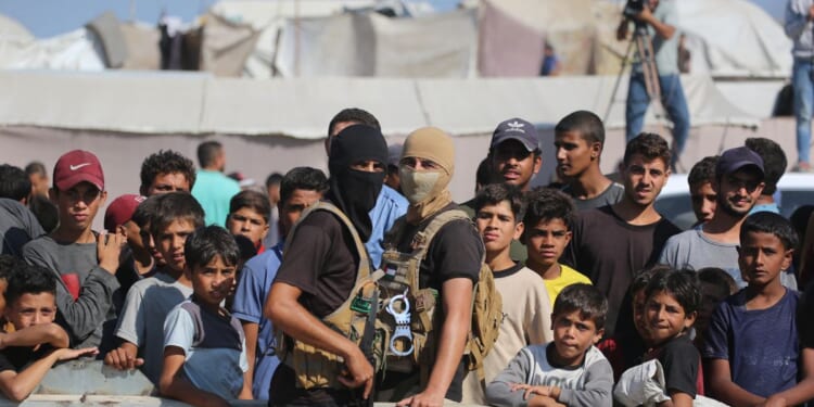 Palestinian militants of the Ezzedine al-Qassam Brigades, the military wing of Hamas, stand guard next to a crowd watching the transfer of released Israeli hostages to the Red Cross in the south of Deir el-Balah in the central Gaza Strip, on Oct. 13, 2025.