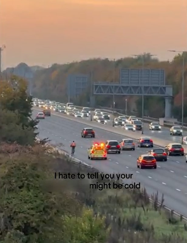 A food delivery cyclist on the M4 motorway in rush hour traffic, with police behind him.