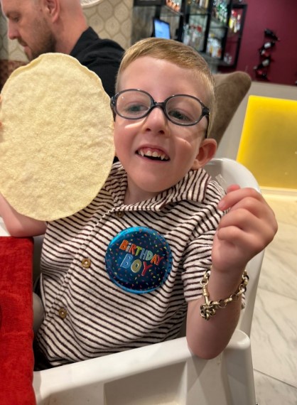 Freddie Michael Webster, a boy wearing a "Birthday Boy" badge, holding a poppadom.