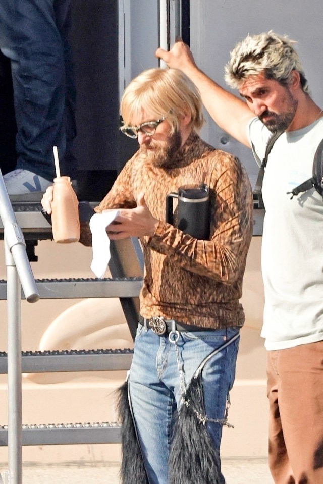 Jonah Hill as an actor portraying a twin on the set of "Cut Off" in a leopard print top, blonde wig, beard, glasses, jeans, and black fringe.