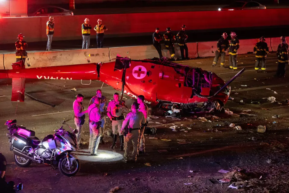 Wreckage of a red medical helicopter on a highway.