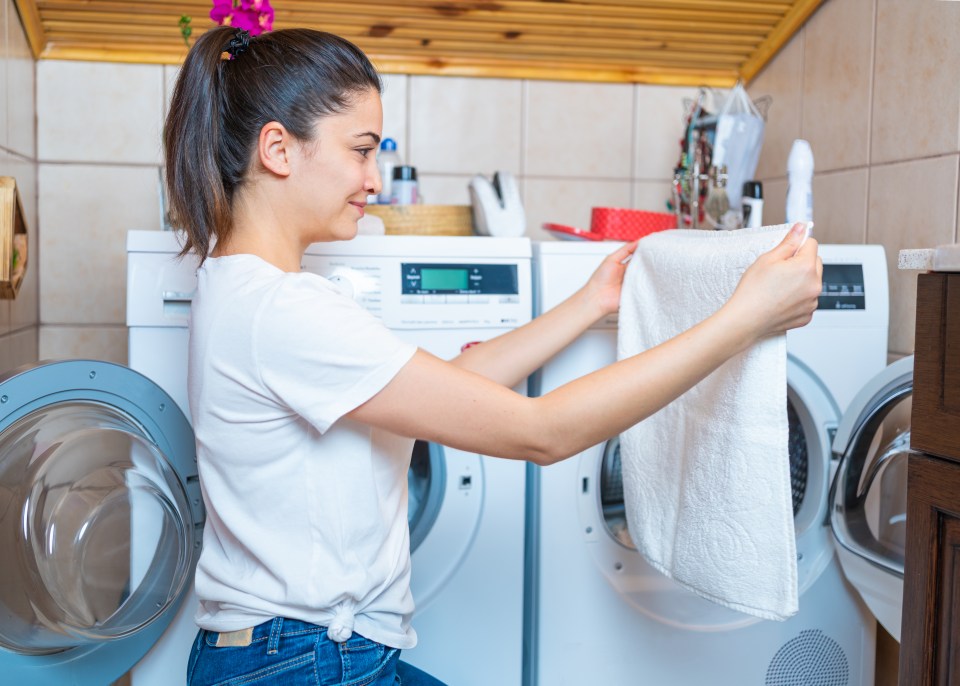 a woman is putting a white towel into a washing machine