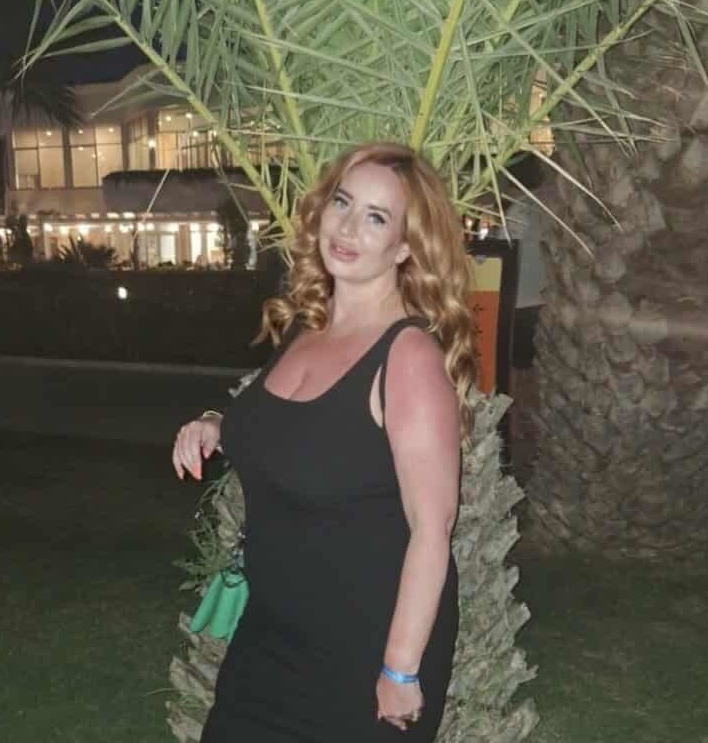 Victoria Miller in a black dress in front of palm trees at night.