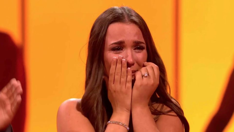 A young woman with long dark hair covering her face with her hands while crying.