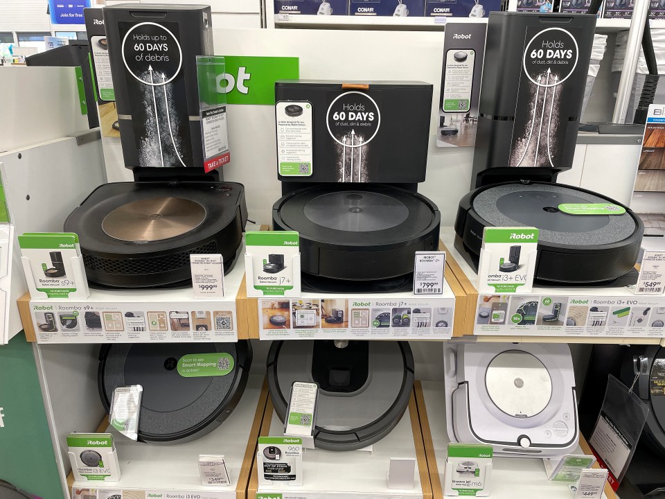 Several Roomba robot vacuums are displayed on shelves in a Bed Bath & Beyond store.