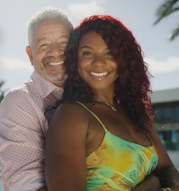 A man with gray hair and a woman with red hair embrace and smile.