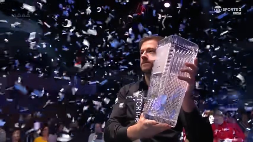 A man holding a crystal trophy while confetti falls.