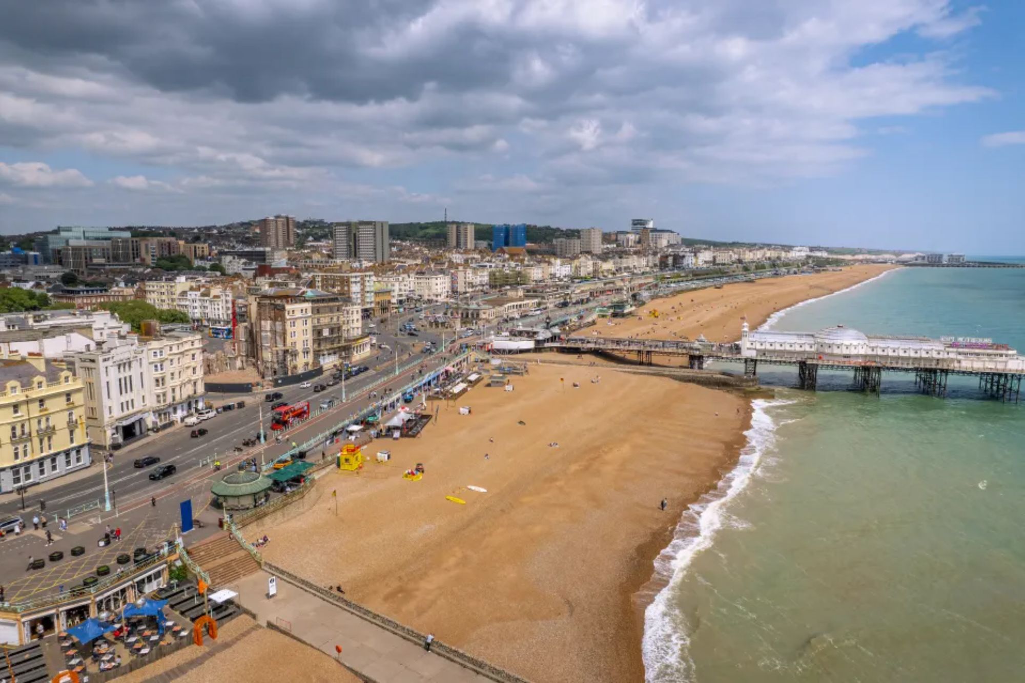 An image collage containing 1 images, Image 1 shows Aerial view of Brighton's beachfront with the Palace Pier extending into the sea, a city skyline in the background, and a wide pebble beach