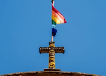 A pride flag stands on top of a Christian cross at a church.