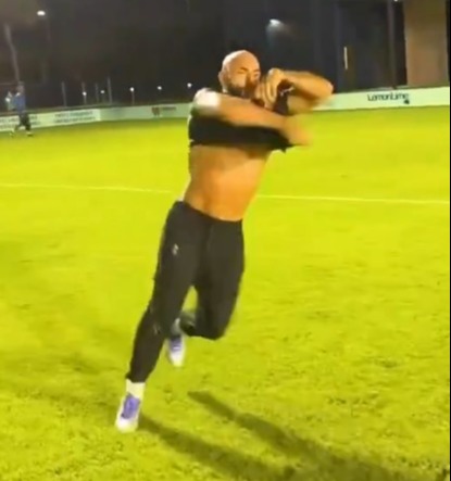 A man runs on a grassy field at night, removing his shirt.