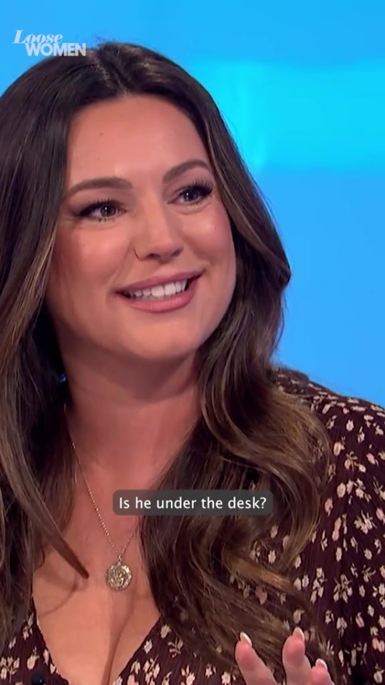 Kelly Brook smiling and wearing a patterned top with a necklace.