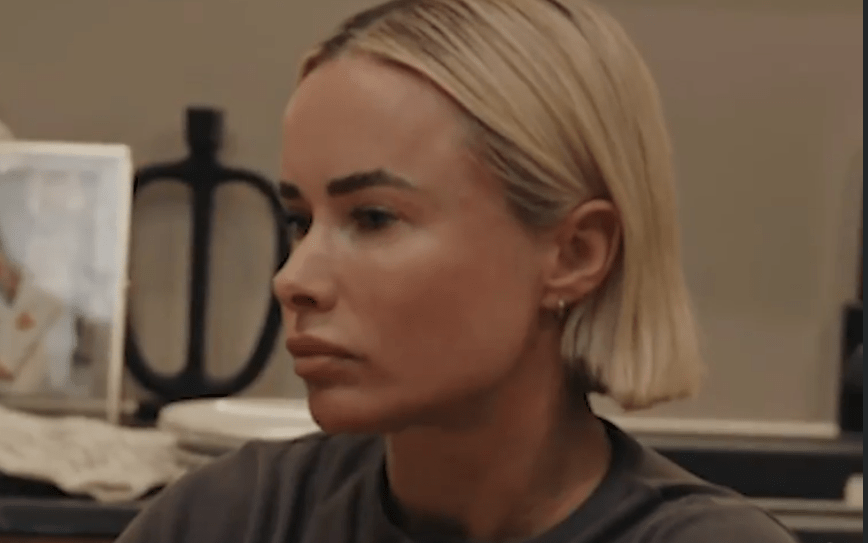 A woman with blonde hair in a short bob, wearing a t-shirt, looks off to the left.