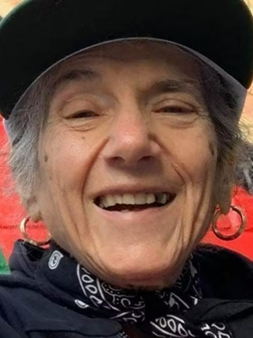 Close-up of a person smiling, wearing a black cap and a bandana.