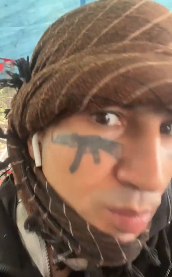 Fayaz Khan wearing a patterned head covering, an earbud, and a rifle tattoo on his cheek.