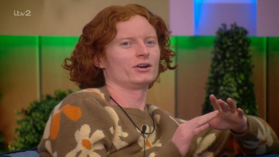 George from Big Brother in a brown, floral sweater, speaking and gesturing with his hands.