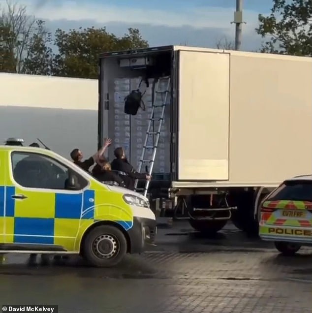 Migrants are guided down a ladder to safety with their possessions after they were discovered hiding inside the large vehicle