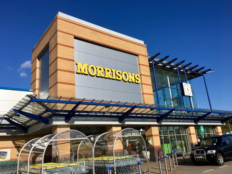 Exterior of a Morrisons supermarket with shopping carts under a clear blue sky.