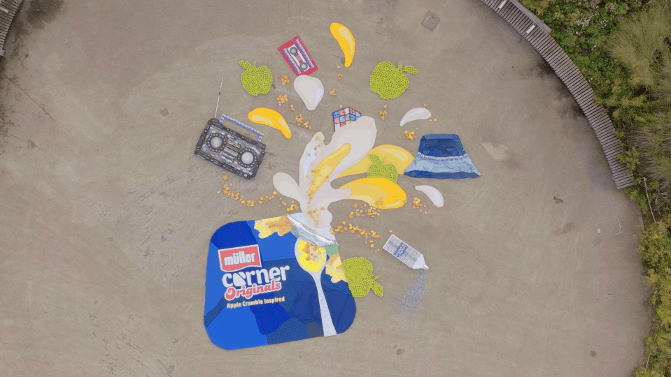 A large Müller Corner Originals Apple Crumble Inspired yogurt container and contents, with 90s themed items like a boombox, cassette tape, and bucket hat.