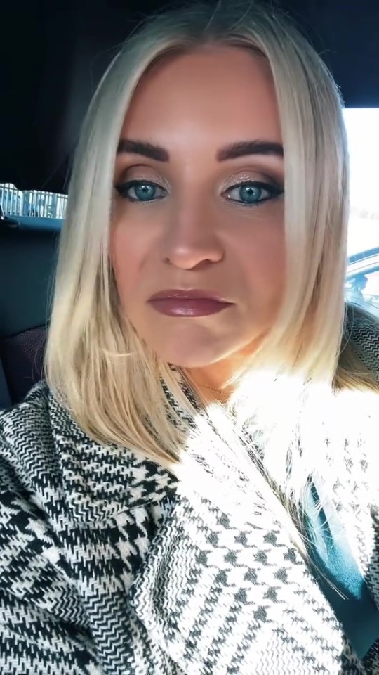 A blonde woman with blue eyes and a houndstooth jacket in a car.