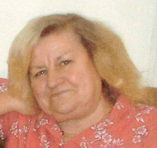 Nora Tait, a woman with blonde hair, wearing a red shirt with a floral pattern.