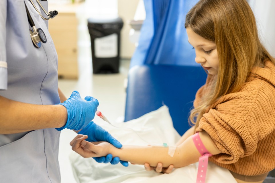 A nurse in blue gloves giving an injection to a young patient.