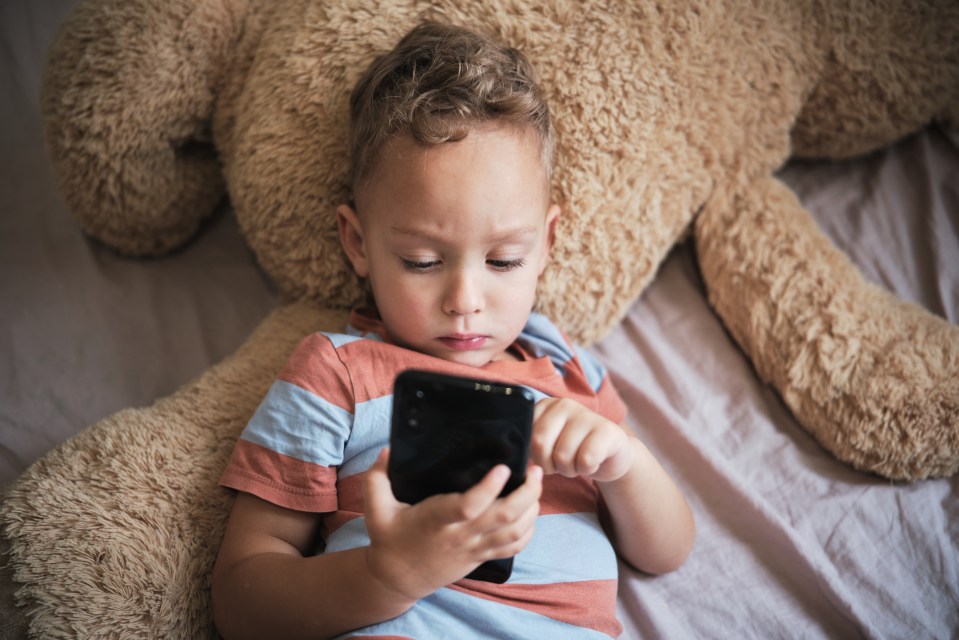 Gadgets and kids. Little child boy using phone at home, kid lying on bed with smartphone playing game or watching cartoons on mobile device