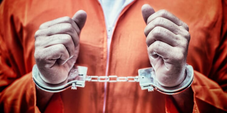 This stock image shows a handcuffed prisoner in an orange jumpsuit.